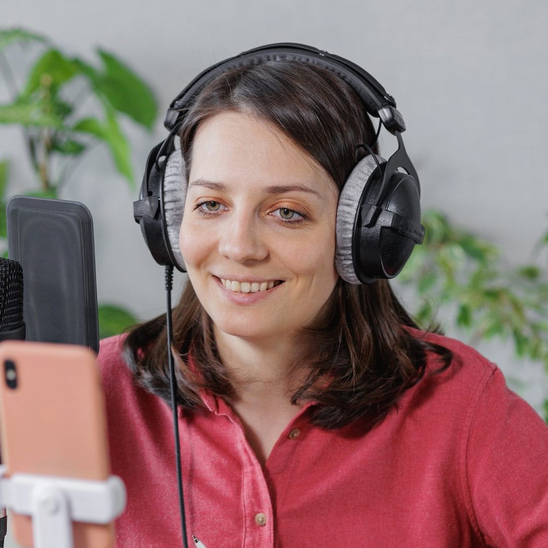 woman in a home office records podcast audio content with a microphone and headphones and a labrador e1688553481834